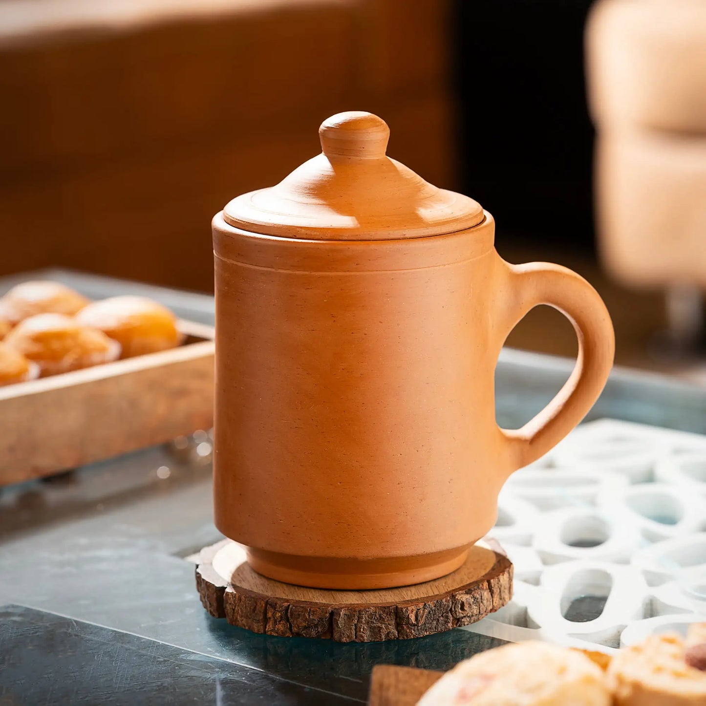 Terracotta mug with lid on a wooden coaster, blurred background