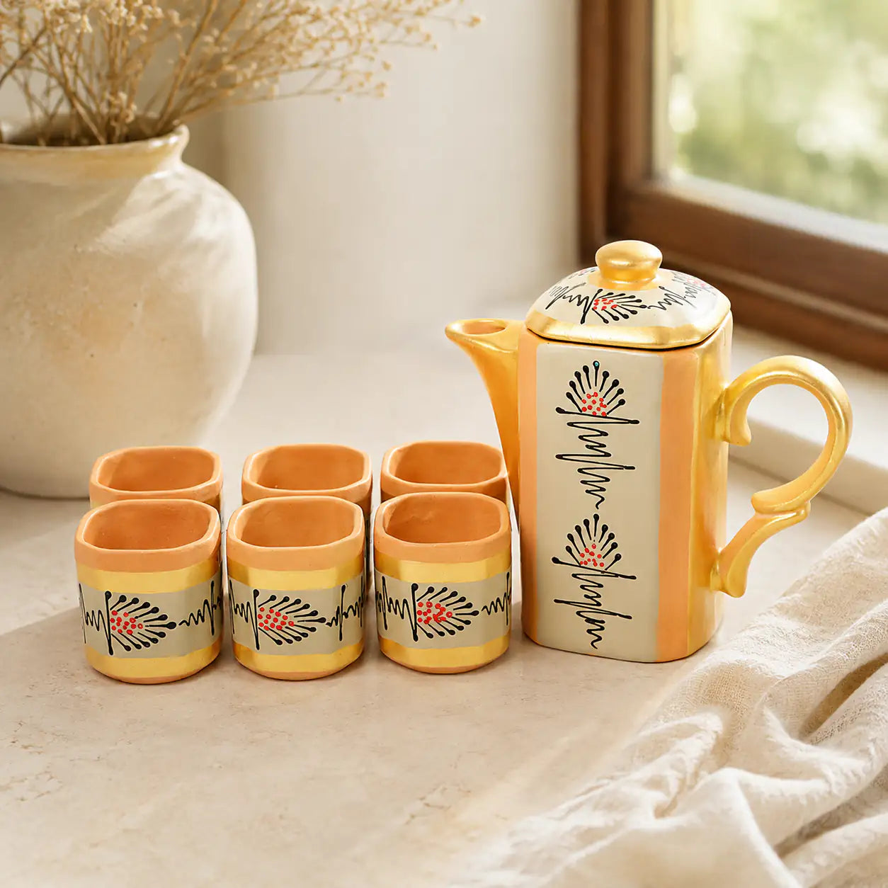 Clay teapot and six cups with decorative patterns on a light surface.