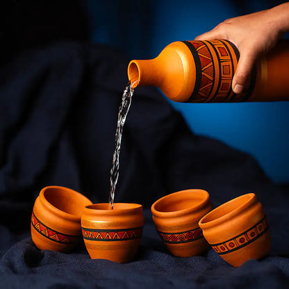Hand pouring water from a decorative terracotta pot into four other similar pots on a dark background.