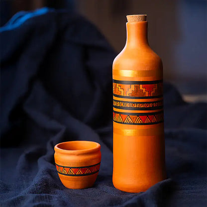 Terracotta bottle and cup with decorative patterns on a dark fabric background