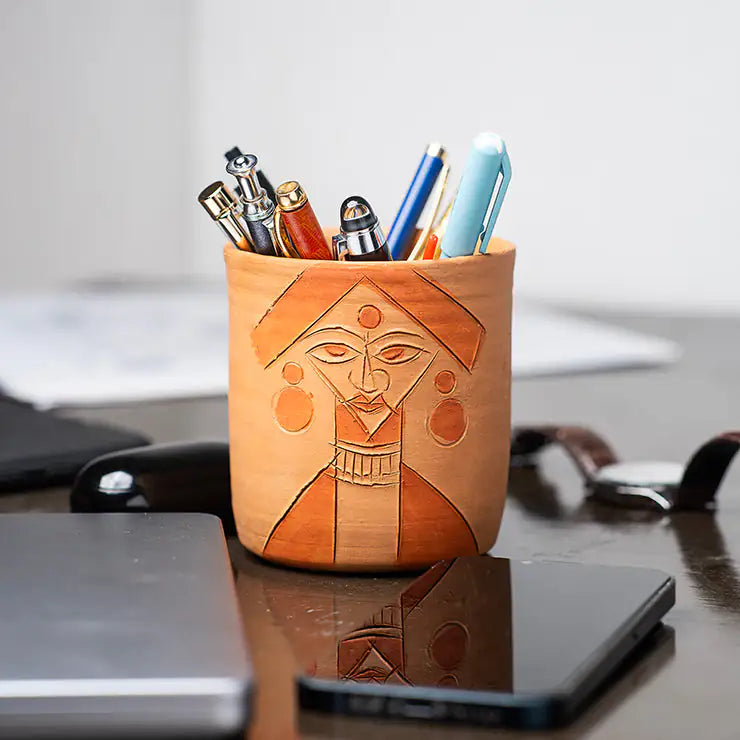 ClayNest handmade terracotta pen stand with carved face-art motif, desk organizer holding pens on a table