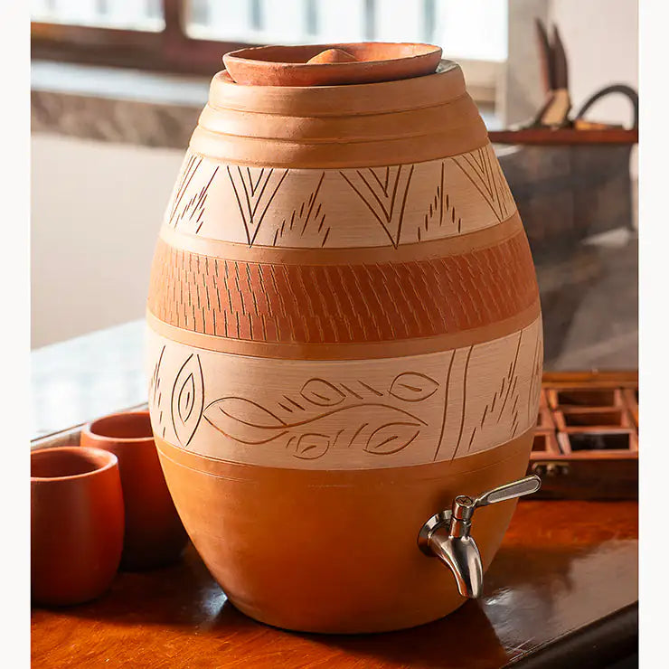 Decorative terracotta water dispenser with engravings on a wooden surface.