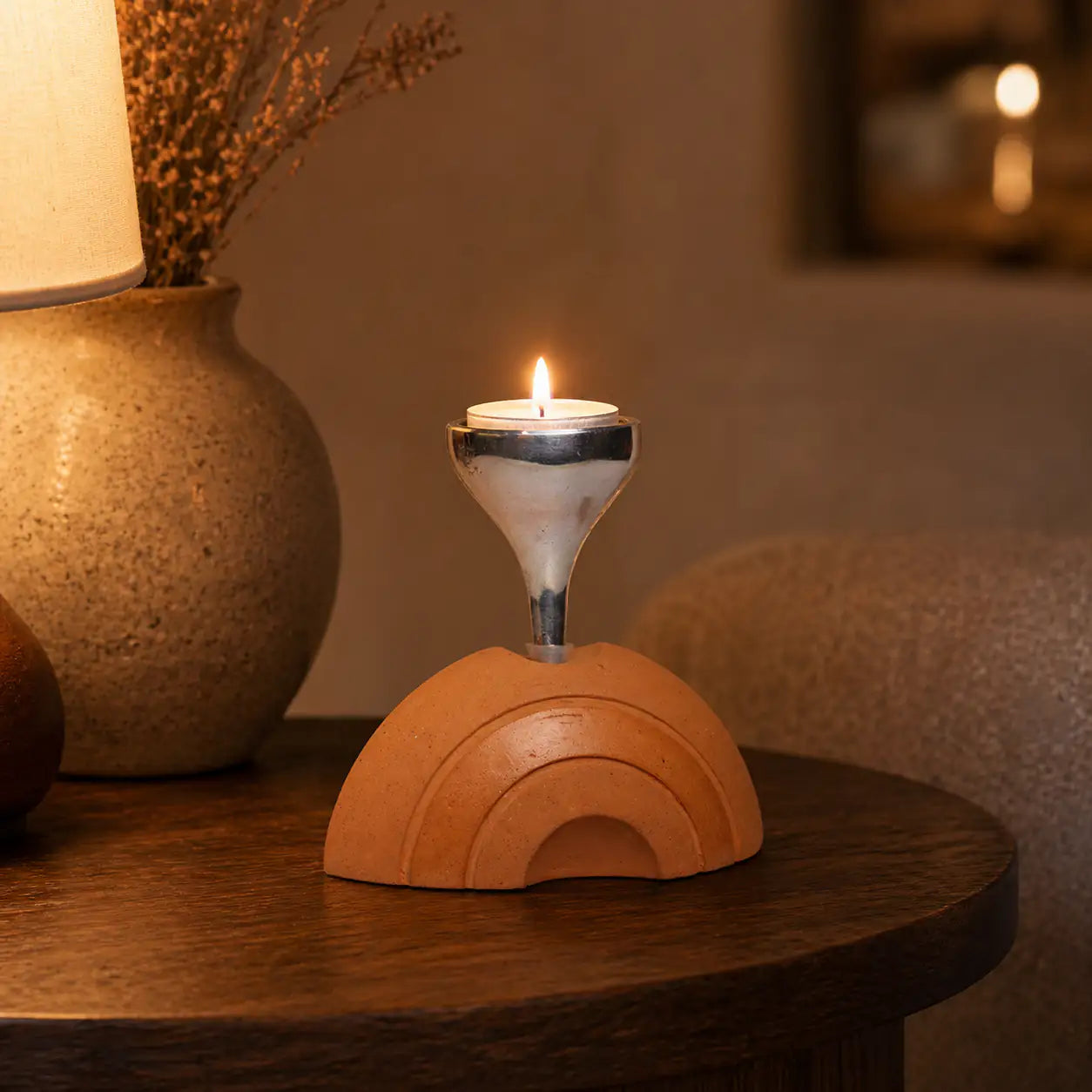 Terracotta tealight stand glowing beside lamp and vase