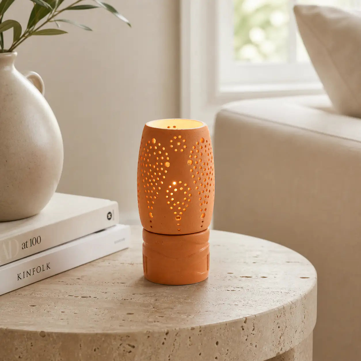 Terracotta tealight holder with cutwork perforation beside vase