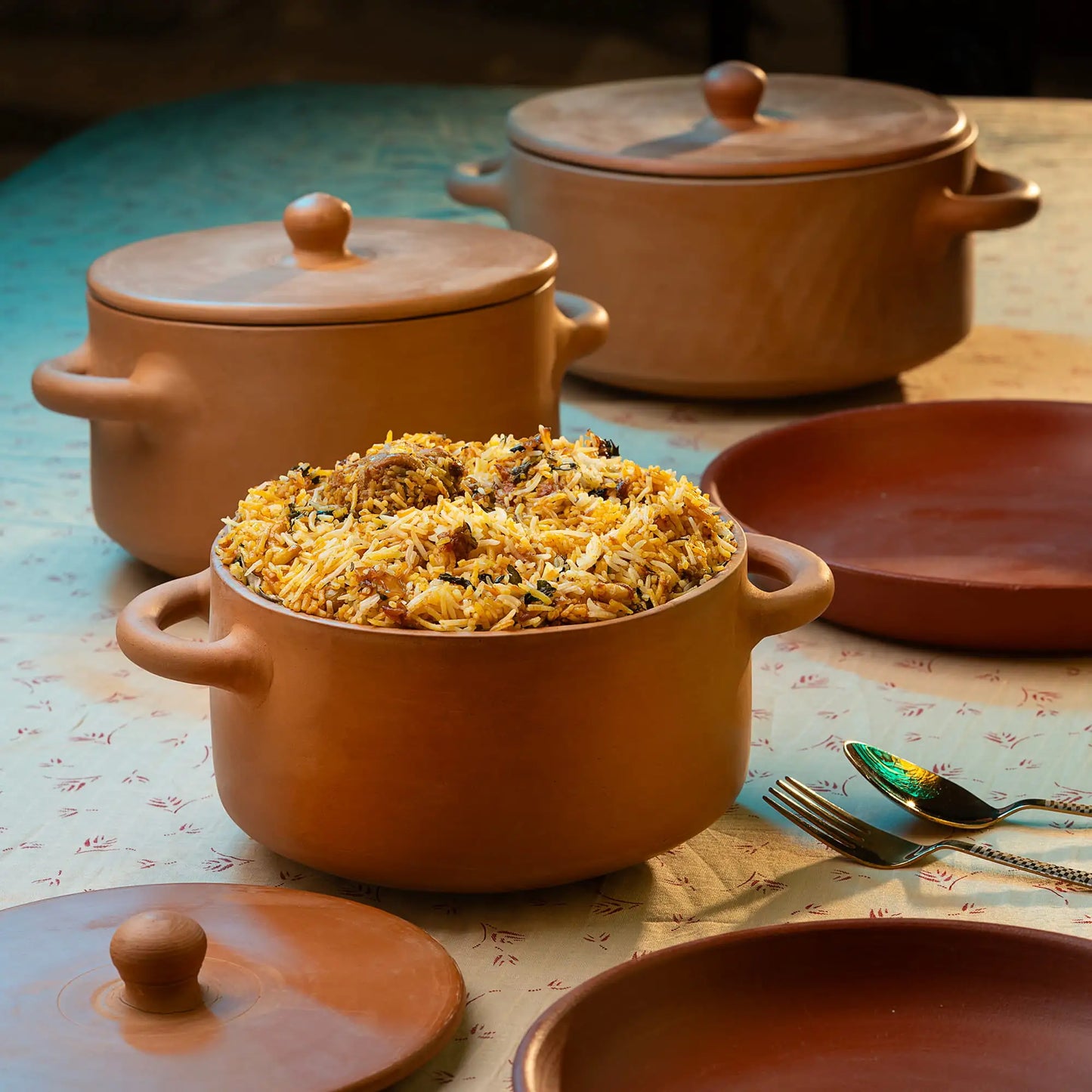 Terracotta pots with food on a table with utensils