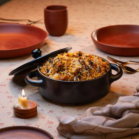 Black Terracotta Casserole dish with rice and meat on a table with ceramic plates and a candle.
