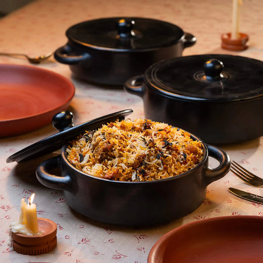 Black Terracotta pot with biryani on a table with candles and plates