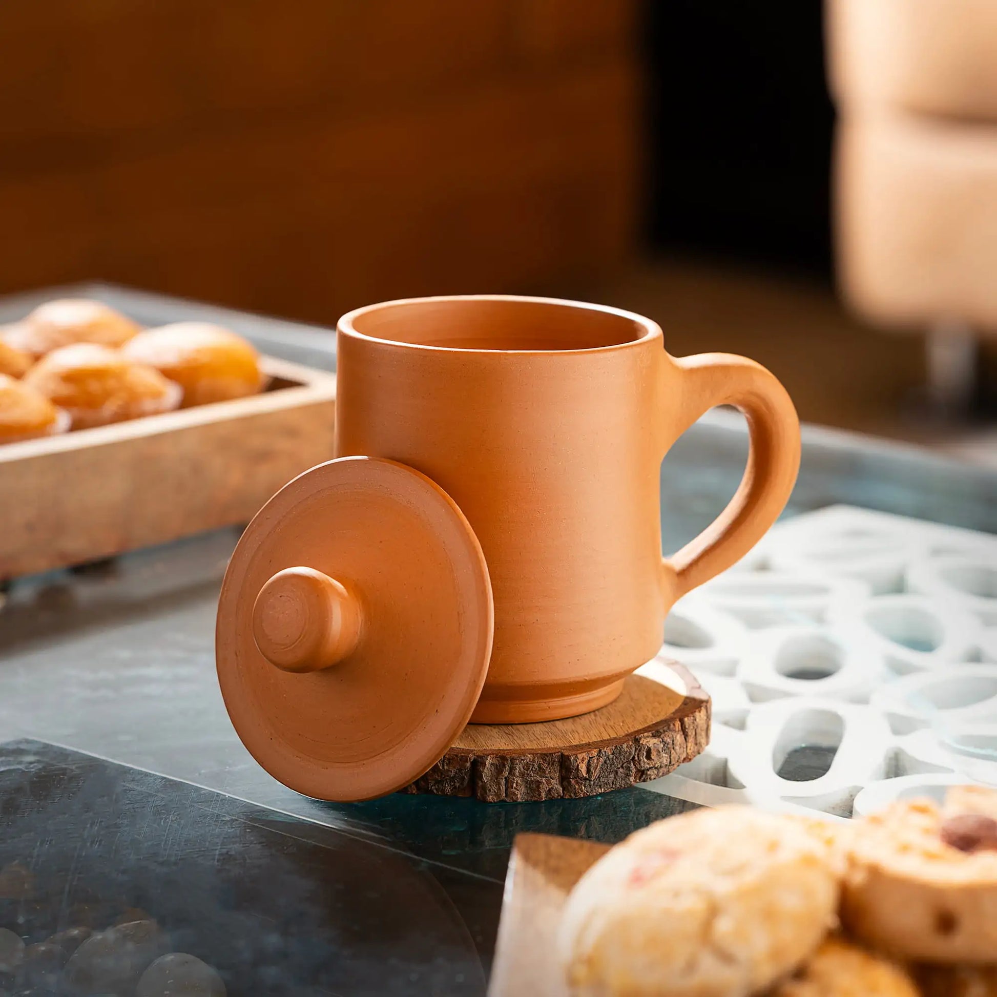 Terracotta mug with lid on a coaster with pastries in the background