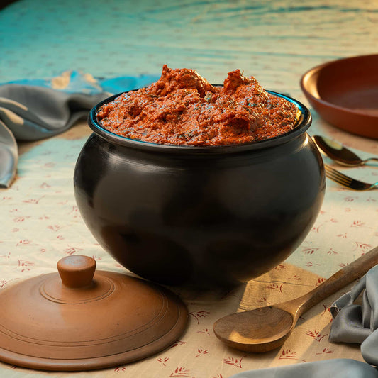 Black Terracotta pot with red curry on a patterned tablecloth
