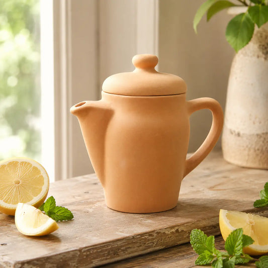 Terracotta teapot on a wooden surface with lemons and mint leaves.