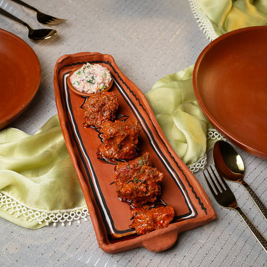 Ceramic dish with meatballs and a side of sauce on a table setting with plates and cutlery.