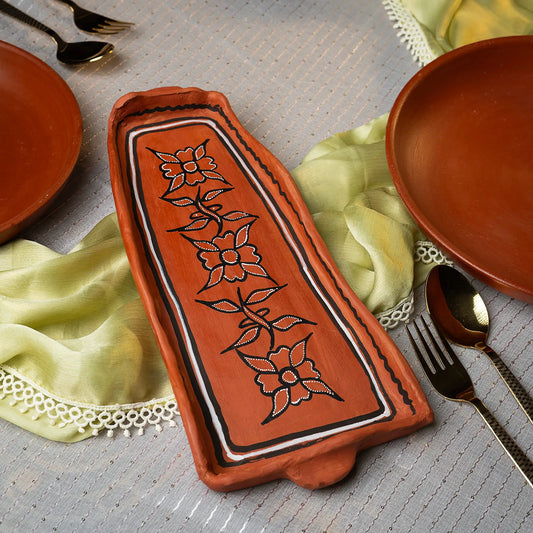 Decorative terracotta tray with floral patterns on a table setting with plates and cutlery.