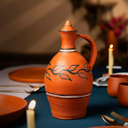 Terracotta pitcher with decorative elements on a table setting with candles and plates.