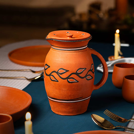 Terracotta pitcher with decorative patterns on a table setting with candles and cutlery.