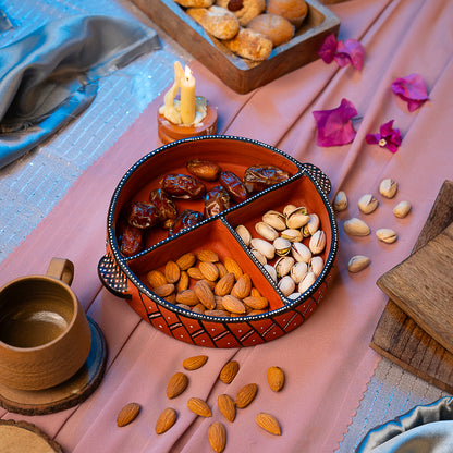 Nuts in a divided Clay bowl on a pink fabric with a candle and cup.