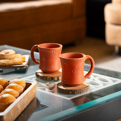 Two terracotta mugs with decorative holes on a glass table with pastries.