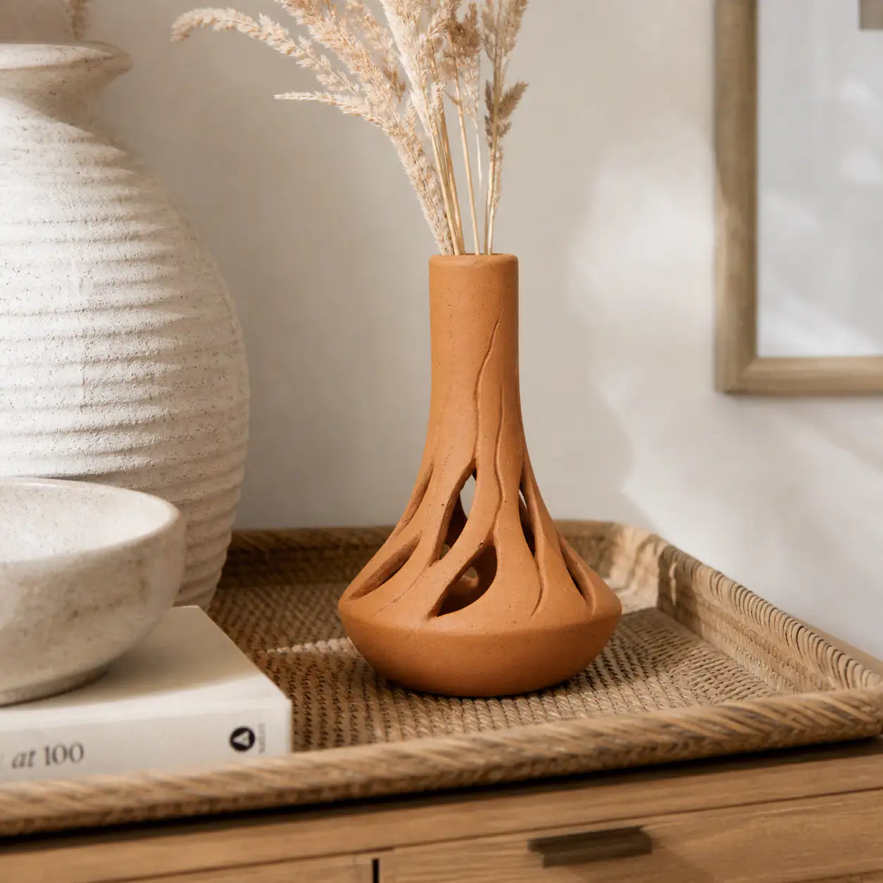 Handmade clay vase placed on woven tray with pampas grass
