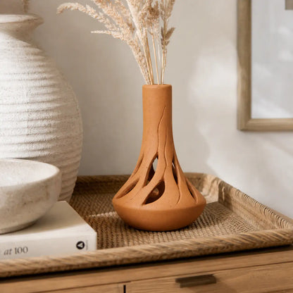 Handmade clay vase placed on woven tray with pampas grass