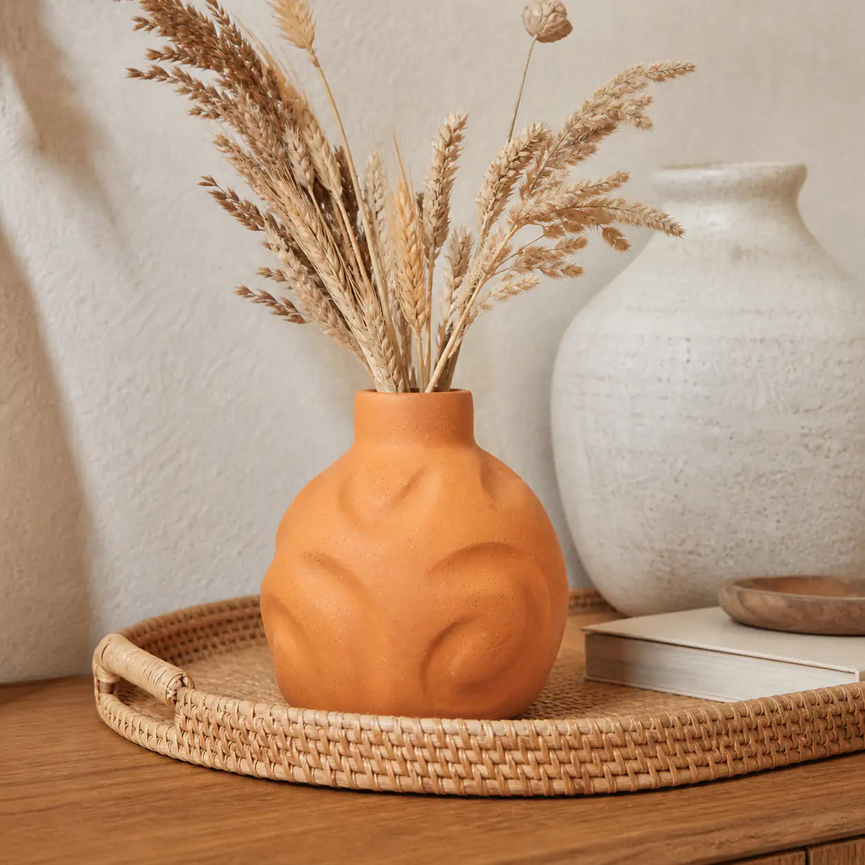 Rounded terracotta décor vase with botanical relief design on woven tray