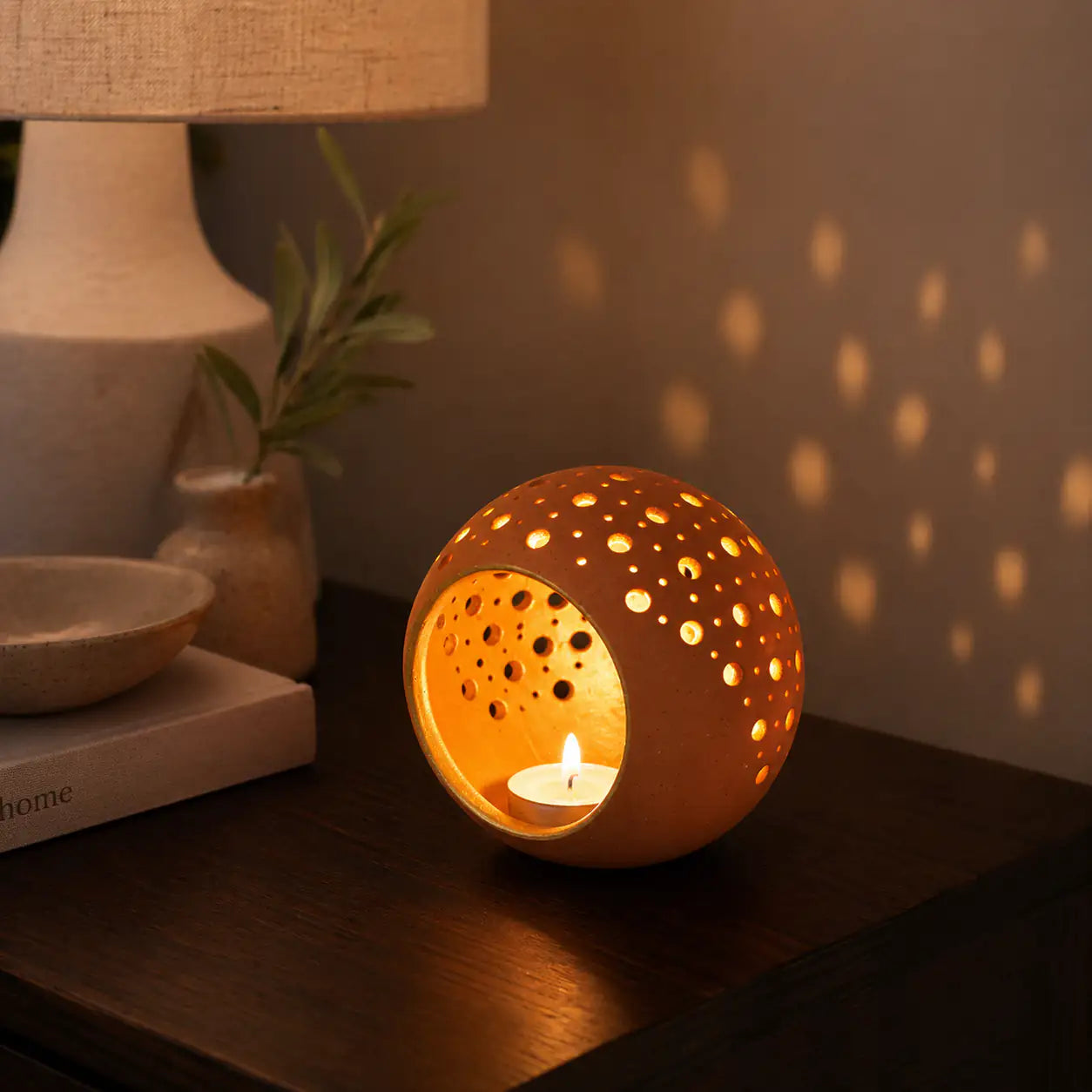 Glowing terracotta tealight holder creating warm light patterns on wall