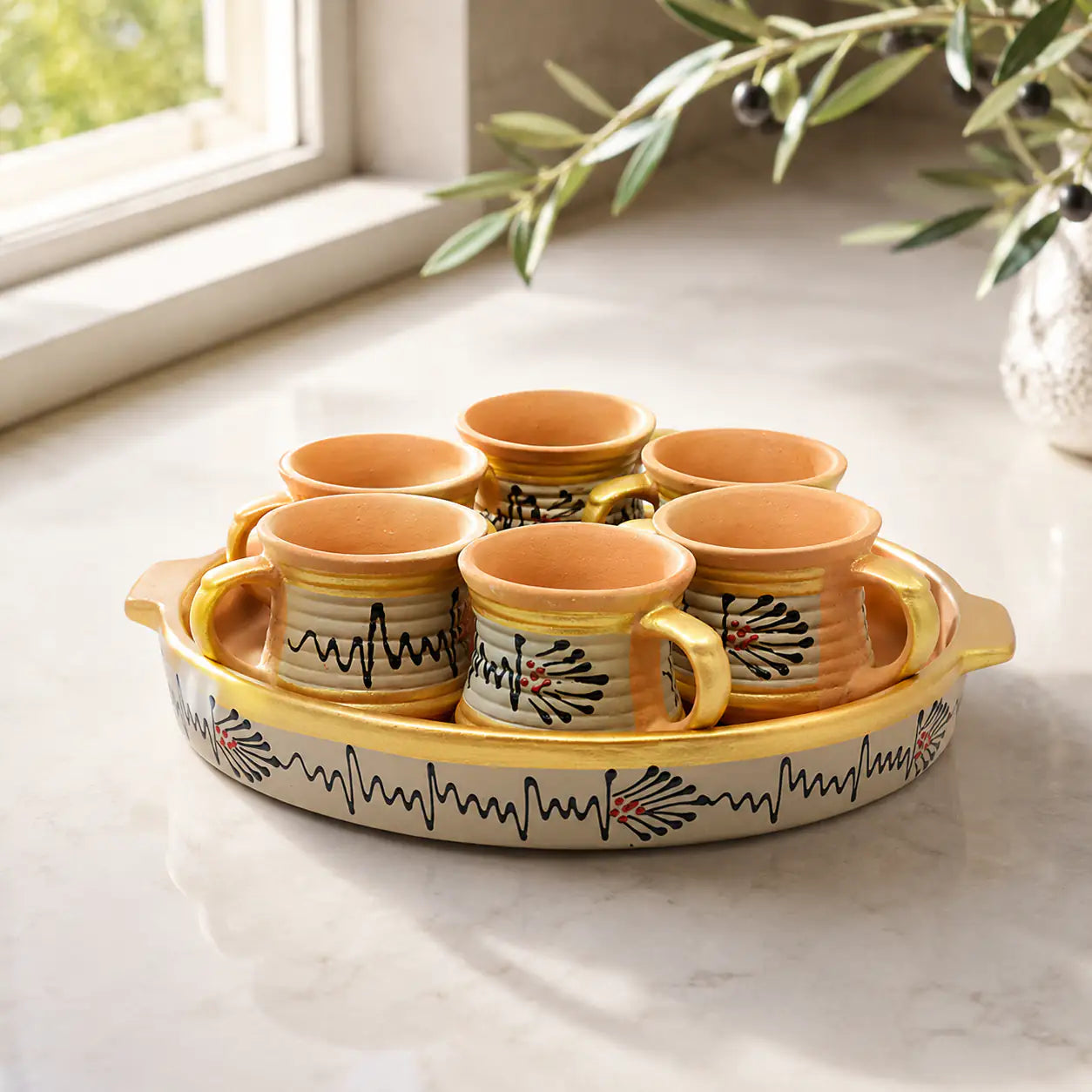 Set of clay cups with a decorative tray on a light surface with a window in the background.