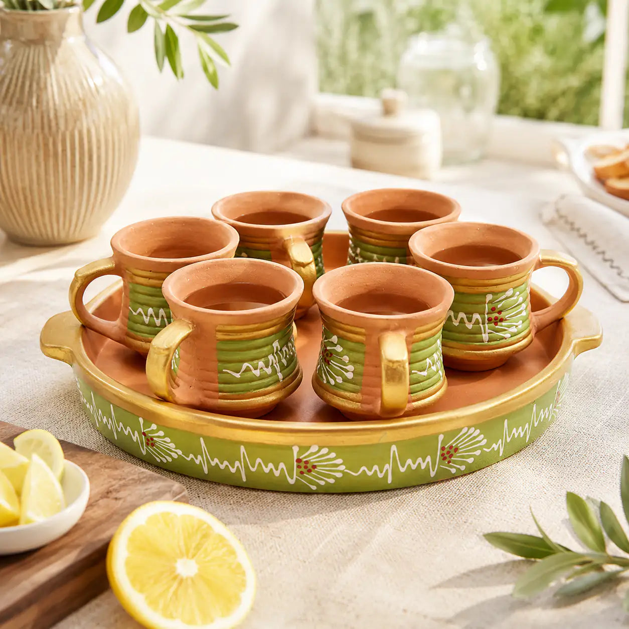 Set of terracotta mugs with a decorative tray on a table with lemon and chips.
