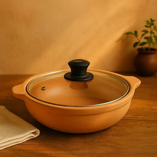 Terracotta pot with a glass lid on a wooden surface, with a plant in the background.